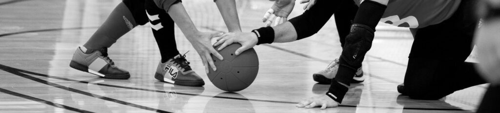 Goalball players place their hands on a goalball on court