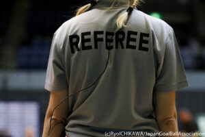 A goalball referee has her back to camera with the words referee on the back of her shirt