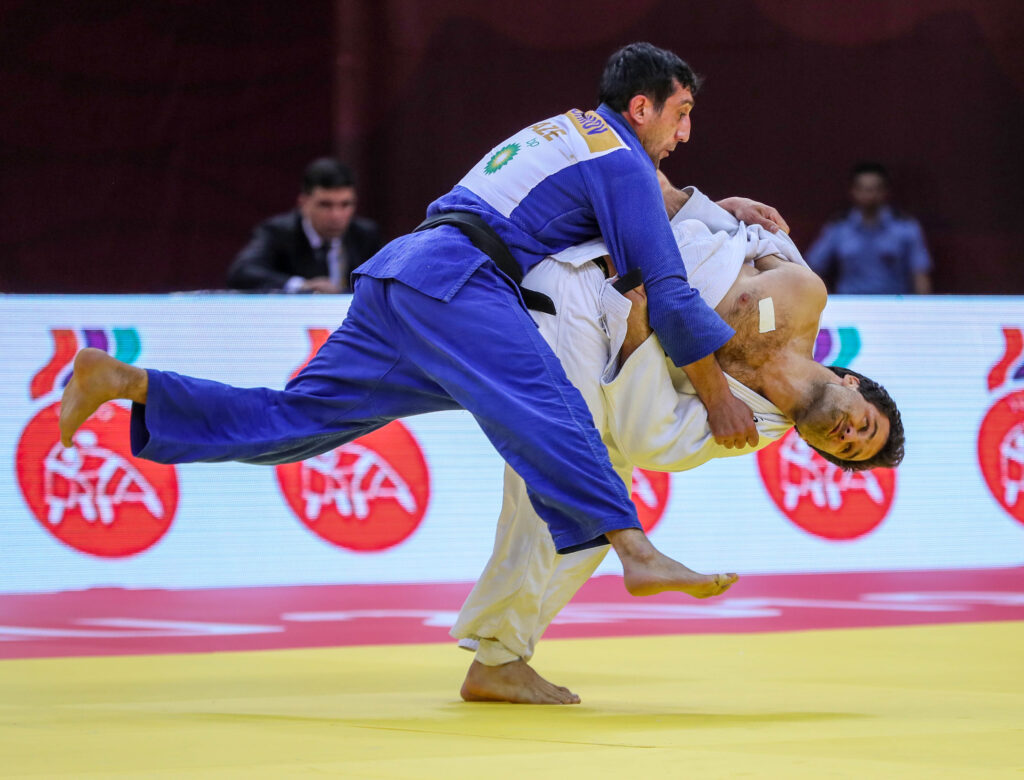 Two judoka with visual impairments are pictured during a throw. One is being hauled over the shoulder of his opponent
