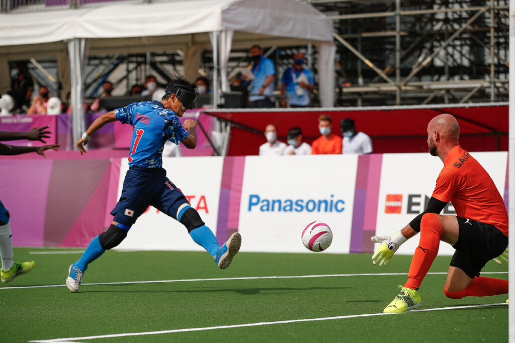 A Japanese blind football player fires the ball towards the goal as the goalkeeper gets ready to save