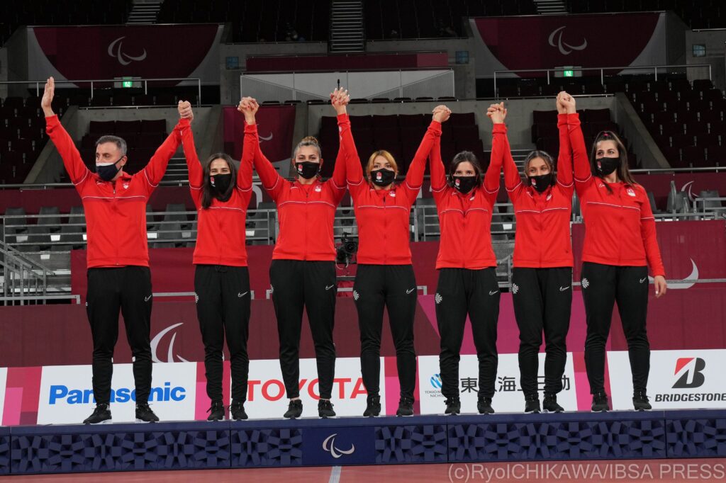 The Turkish women's goalball team stand on the podium with their arms in the air