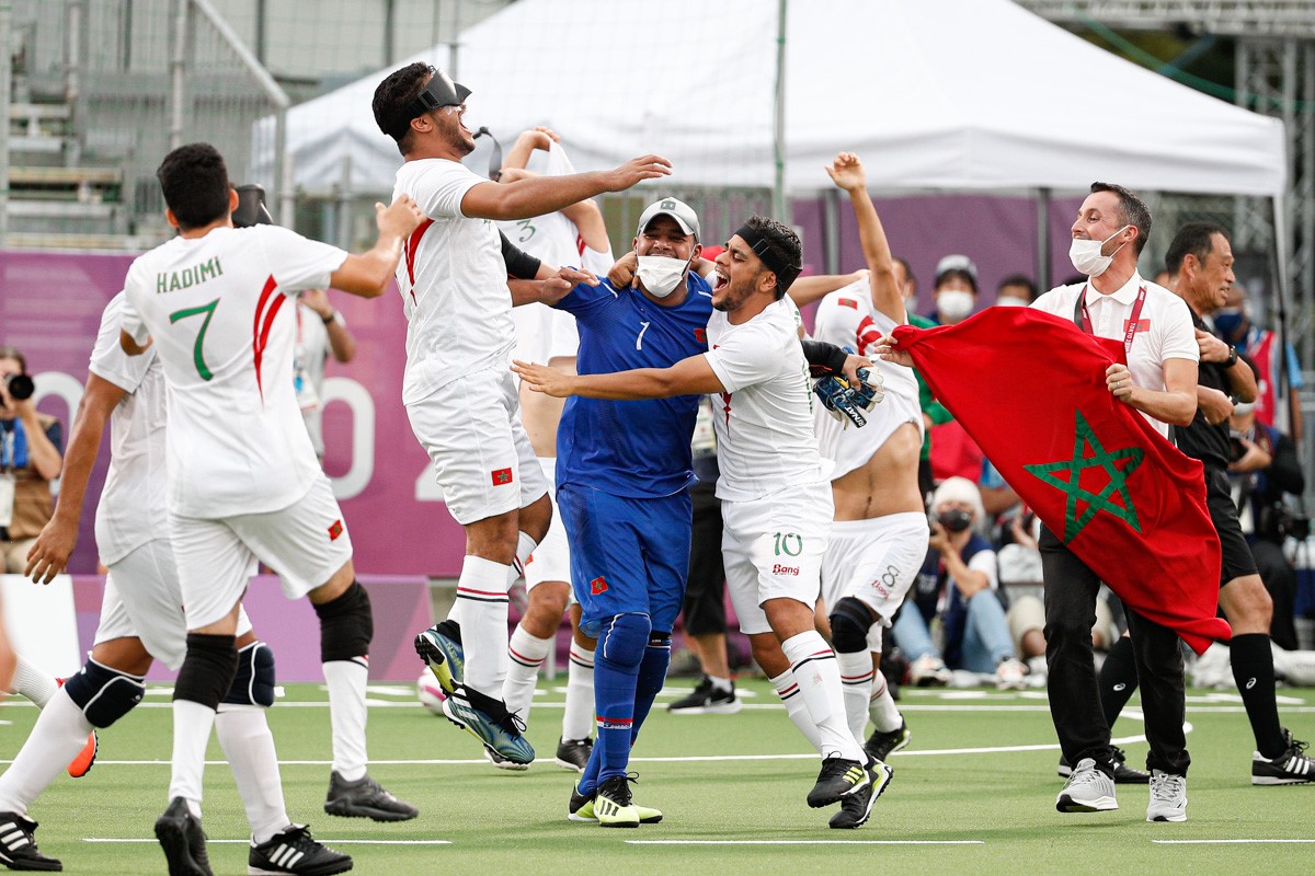 Moroccan blind football players jump high into the air as their team staff run onto the pitch with their national flags during the blind football bronze medal match at Tokyo 2020
