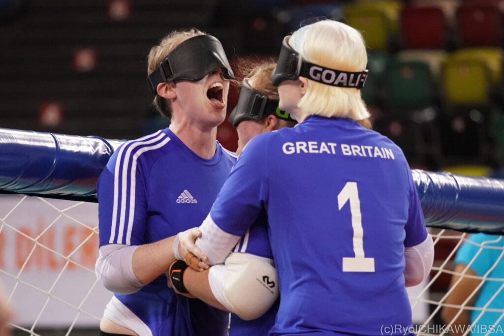 A British goalball player screams in delight as her teammates gather around her to embrace