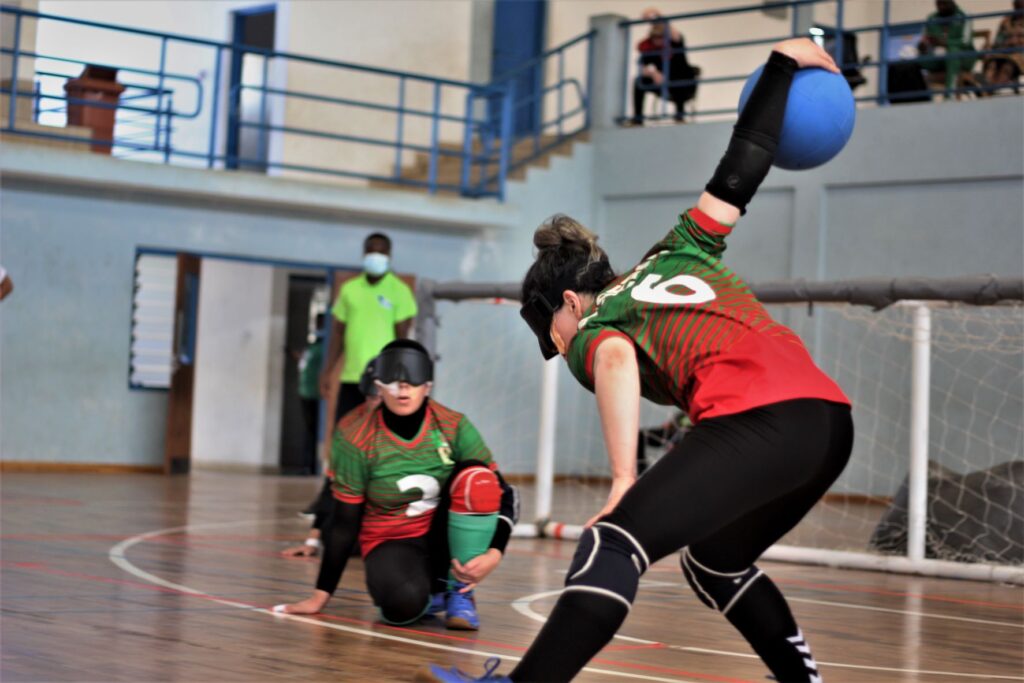 A femal goalball player from Algeria holds the ball high out behind her during a throw