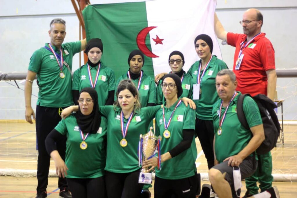 The Algerian women's team and their coaches pose with their medals around their necks as their coaches hold their national flag behind them
