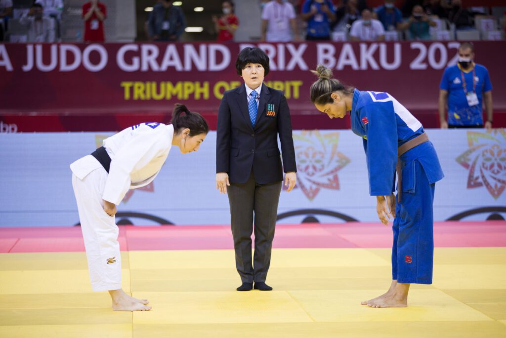 Two female judoka bow at the end of their fight whilst the referee stands in the middle